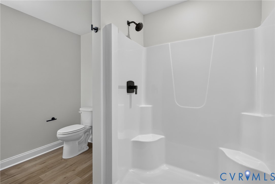 White shower enclosure with integrated shelving and seating, matte black shower fixtures, wood-finish flooring, and white toilet White shower enclosure with integrated shelving and seating, matte black shower fixtures, wood-finish flooring, and white toilet