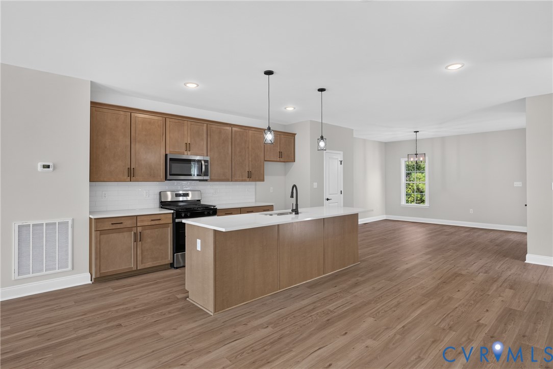 Open-concept kitchen with wood-finish flooring, recessed lighting, and a kitchen island with a built-in sink