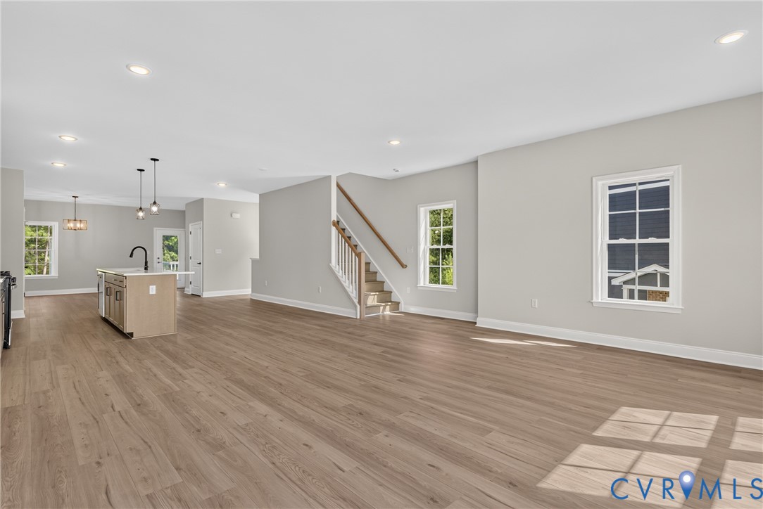 Open-concept living area featuring wood-finish flooring, recessed lighting, a central kitchen island with a dark faucet, and a stairway with white balusters