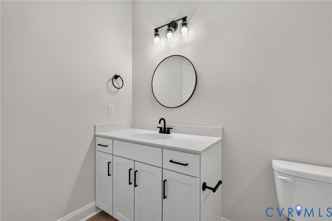 White vanity with black hardware, white countertop, round mirror, and wall-mounted light fixture