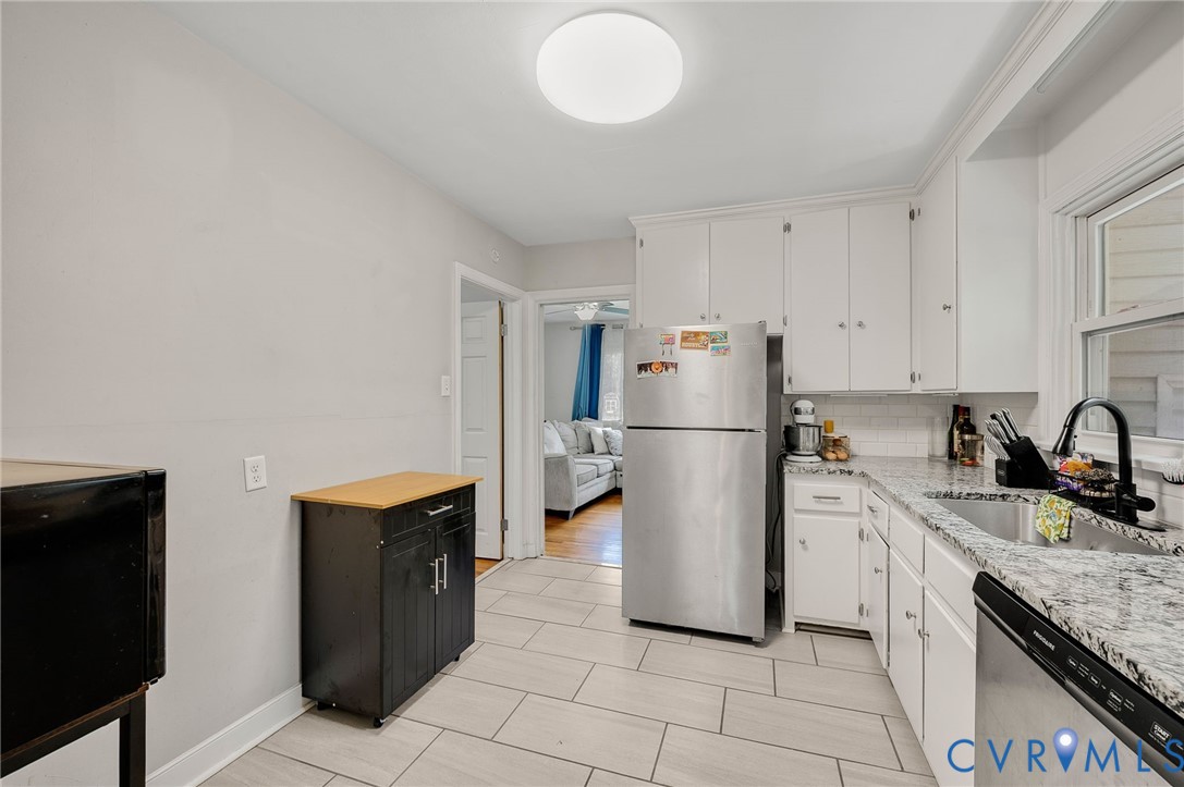 Kitchen featuring tile flooring, white cabinetry, a stainless steel refrigerator, and a stainless steel sink with a black faucet