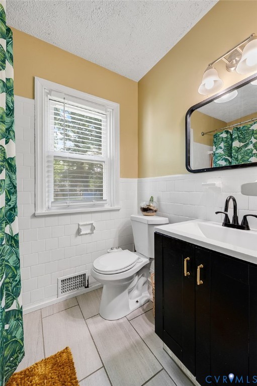 White subway tile wainscoting, light wood-look tile flooring, black vanity with gold-tone hardware, and a framed mirror