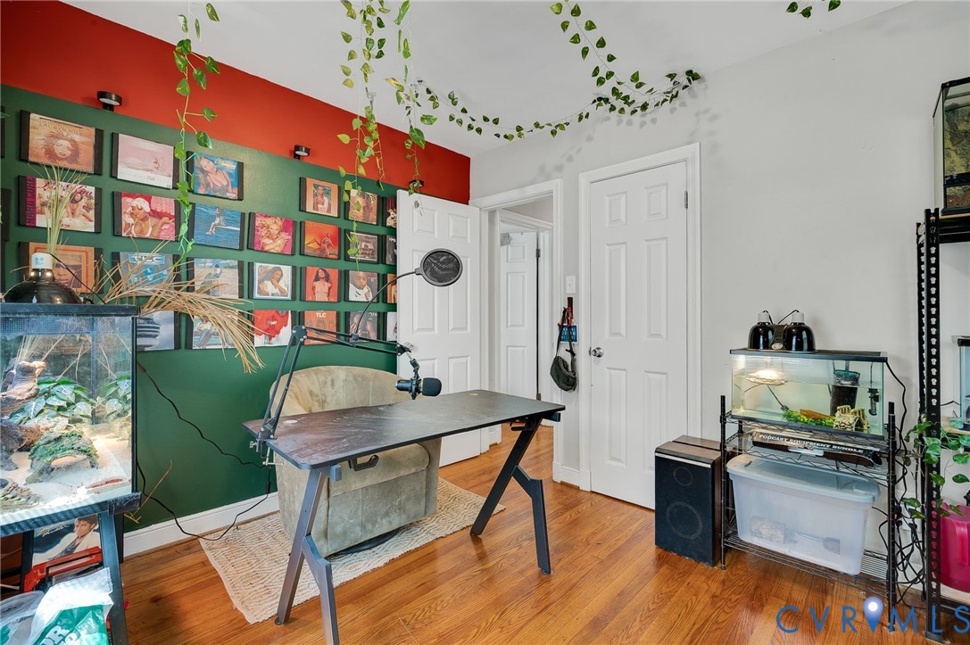 Creative home office featuring warm wood-finish flooring, custom green built-in wall shelving with red accent paneling, white six-panel closet doors, and black hardware accents throughout the space