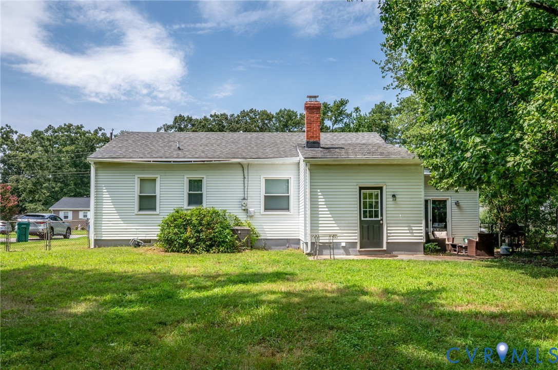 Rear exterior featuring white horizontal siding, a red brick chimney, a dark paneled door with glass inserts, and a concrete patio Rear exterior featuring white horizontal siding, a red brick chimney, a dark paneled door with glass inserts, and a concrete patio
