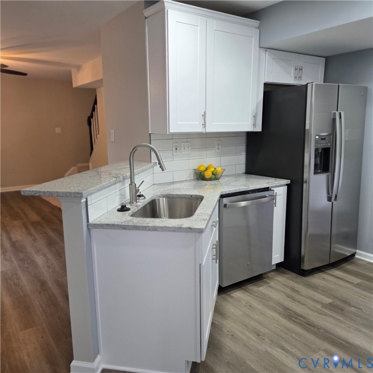 Modern kitchen featuring white shaker cabinetry, stainless steel appliances, a subway tile backsplash, light-colored countertops, and wood-finish flooring