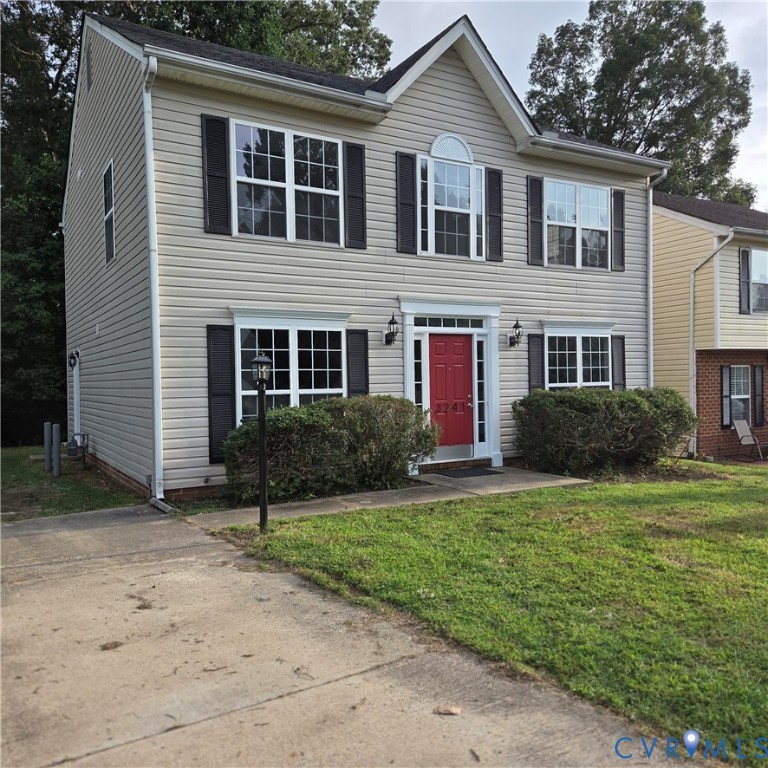 Two-story residence featuring light-colored siding, contrasting dark shutters, and a vibrant red entry door