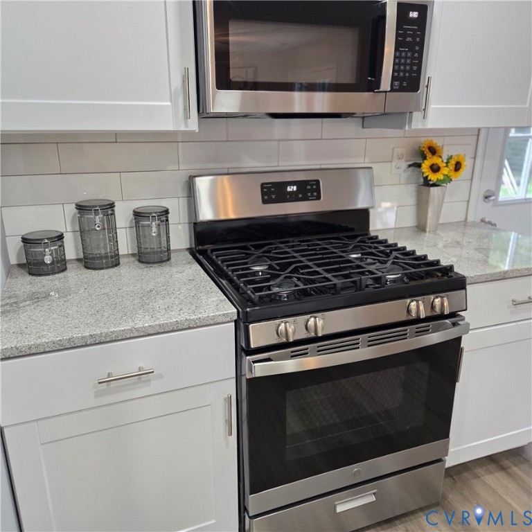 Stainless steel gas range with coordinating microwave, white subway tile backsplash, light-toned countertops, and white shaker-style cabinetry