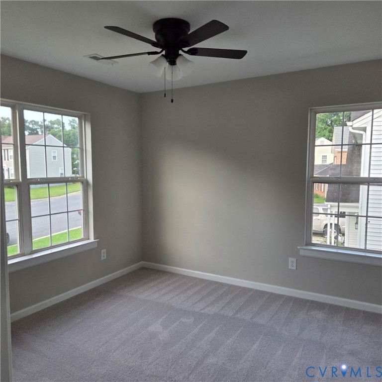 Neutral wall paint, ceiling fan with integrated lighting, two windows with grid patterns, and plush carpet flooring
