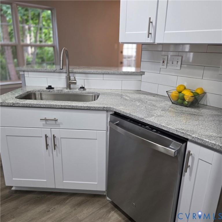Modern kitchen featuring white shaker-style cabinetry, quartz countertops with waterfall edge detail, stainless steel single-basin undermount sink with chrome gooseneck faucet, subway tile backsplash, and stainless steel dishwasher