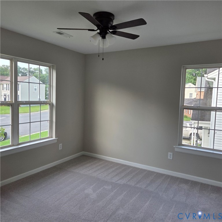 Neutral wall tones, gray carpeting, a ceiling fan with integrated lighting, and two windows with grid patterns