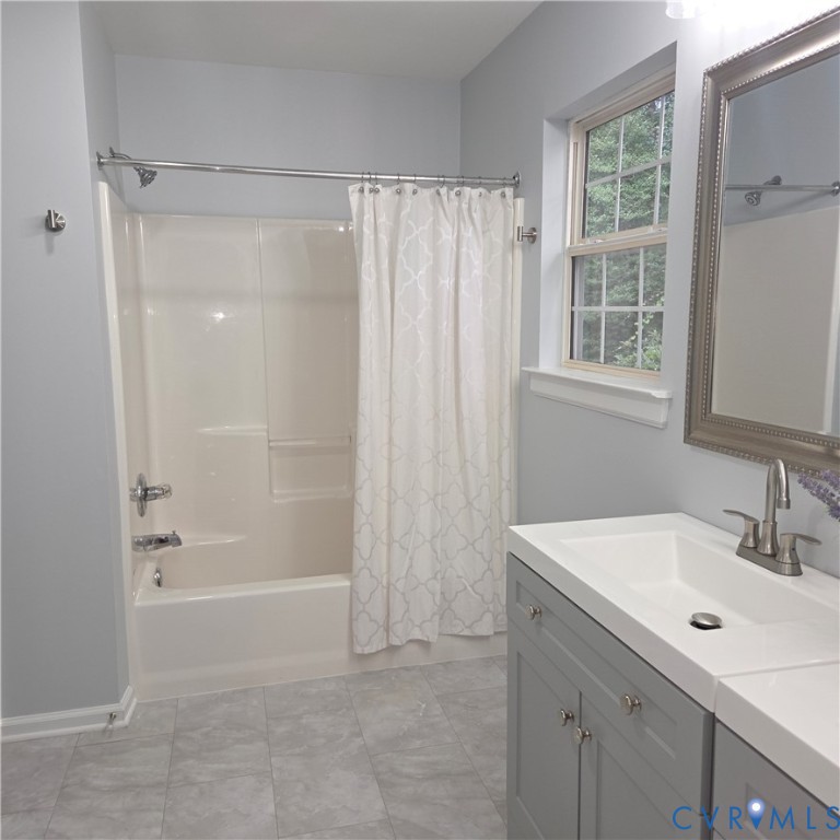 Integrated tub/shower combination, gray vanity with white integrated sink, chrome fixtures, and a window with natural light