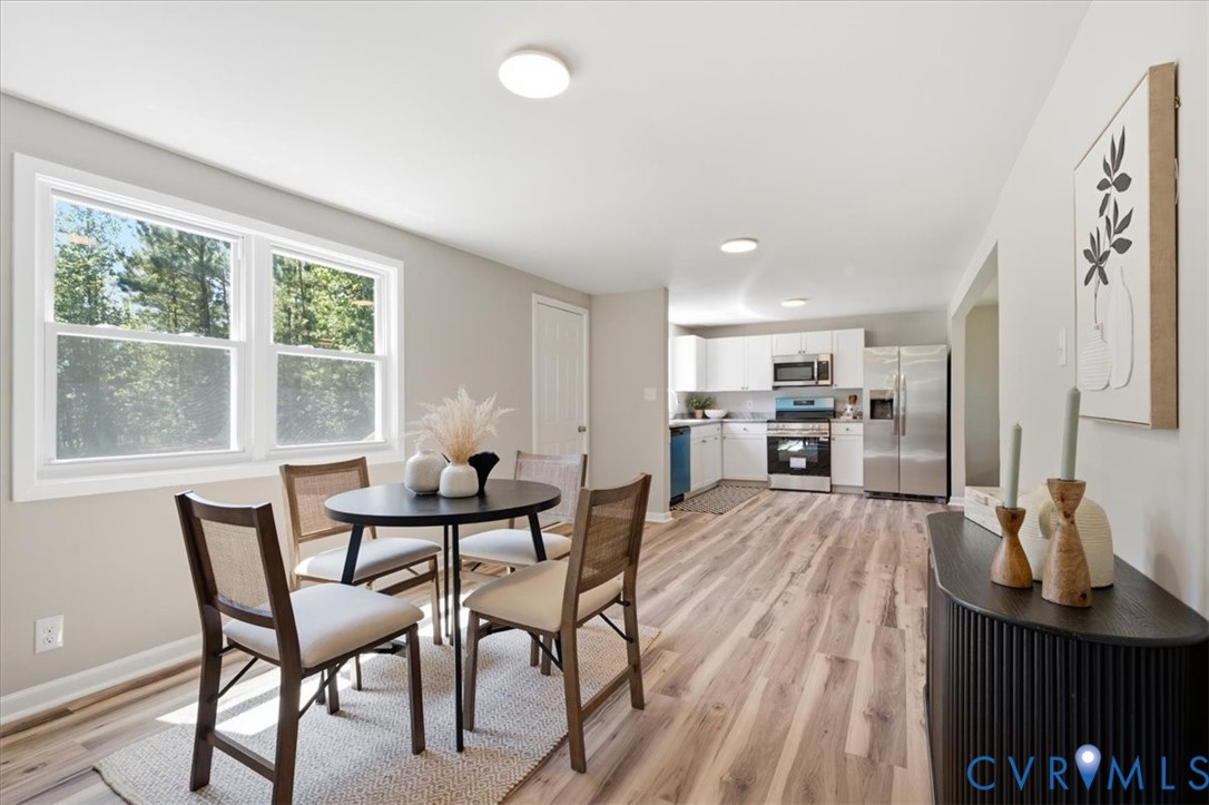 Open-concept kitchen and dining area featuring wood-finish flooring, white cabinetry, stainless steel appliances, and ample natural light