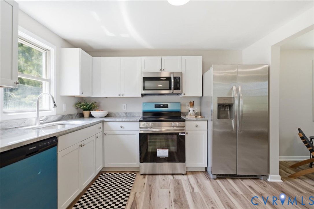 Kitchen featuring white cabinetry, light-toned countertops, stainless steel appliances, and wood-finish flooring