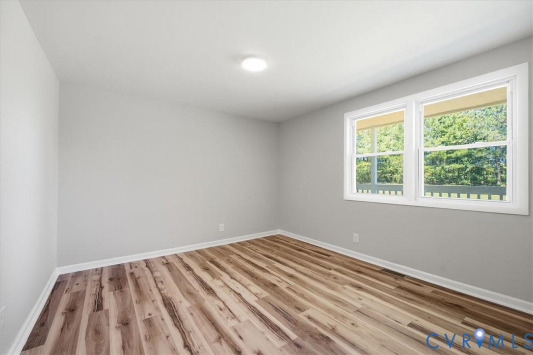 Bright, light-filled bedroom featuring newly installed wood-finish flooring, neutral painted walls, and dual casement windows with natural light exposure