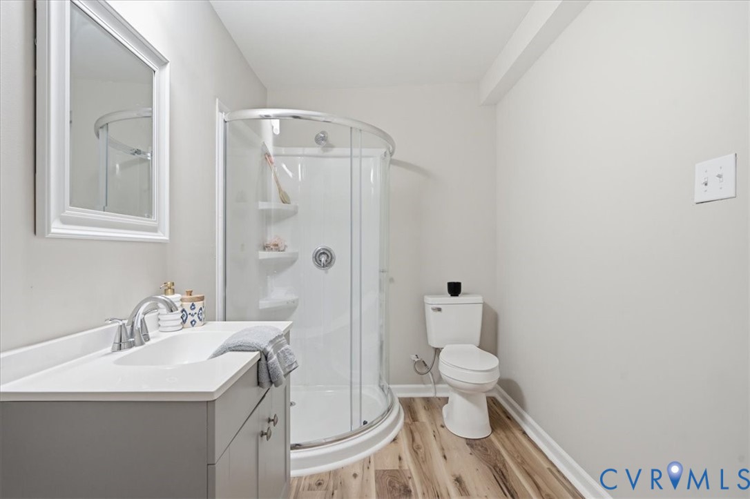 Wood-finish flooring, white walls, and a curved glass shower enclosure define this bathroom