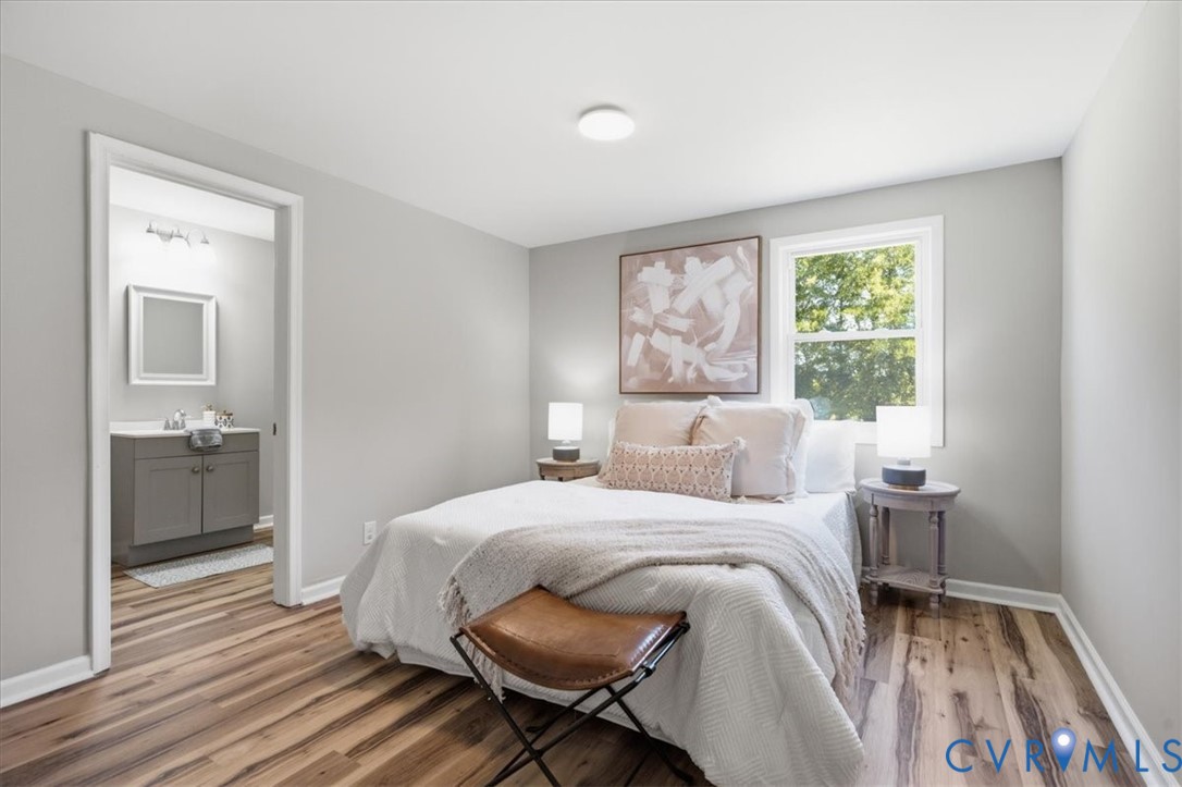 Wood-finish flooring, light grey painted walls, ceiling-mounted light fixture, window with white trim, and a full bathroom with a grey vanity