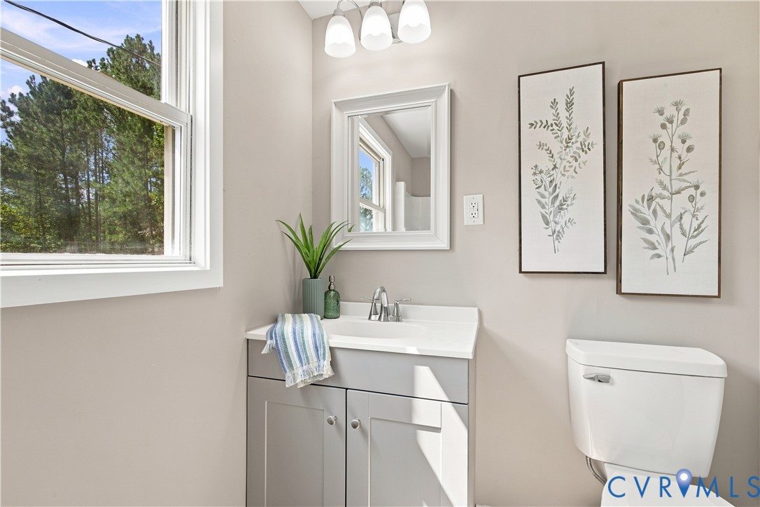 White-framed window, gray vanity with integrated sink, chrome-finish faucet, wall-mounted mirror, and a white toilet