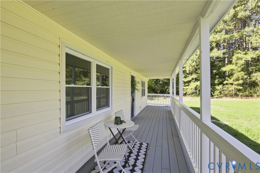 Expansive covered porch with white railings, a gray wood-finish floor, and light-colored siding