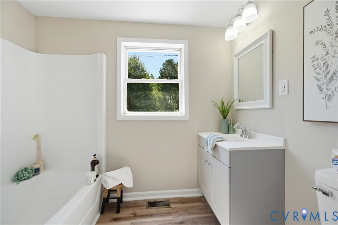 Integrated bathtub with shower, single window, wood-finish flooring, vanity with white countertop, and wall-mounted light fixture