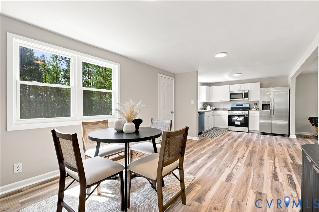 Open-concept kitchen and dining area featuring wood-finish flooring, white cabinetry, stainless steel appliances, and a large window