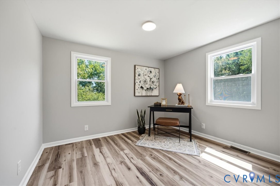 Bright, light-filled room with dual casement windows featuring white frames, recessed ceiling lighting, and wide-plank wood-finish flooring