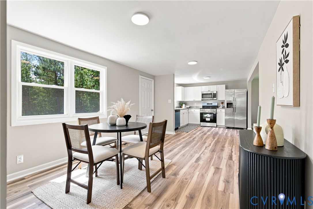 Open-concept living space featuring wood-finish flooring, recessed lighting, and a kitchen with white cabinetry and stainless steel appliances