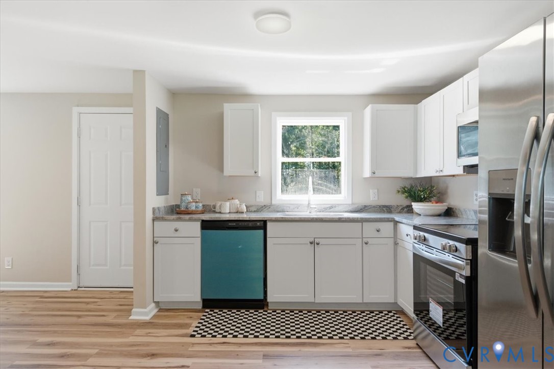 Kitchen featuring white cabinetry, light-toned wood-finish flooring, stainless steel appliances, and a window above the sink