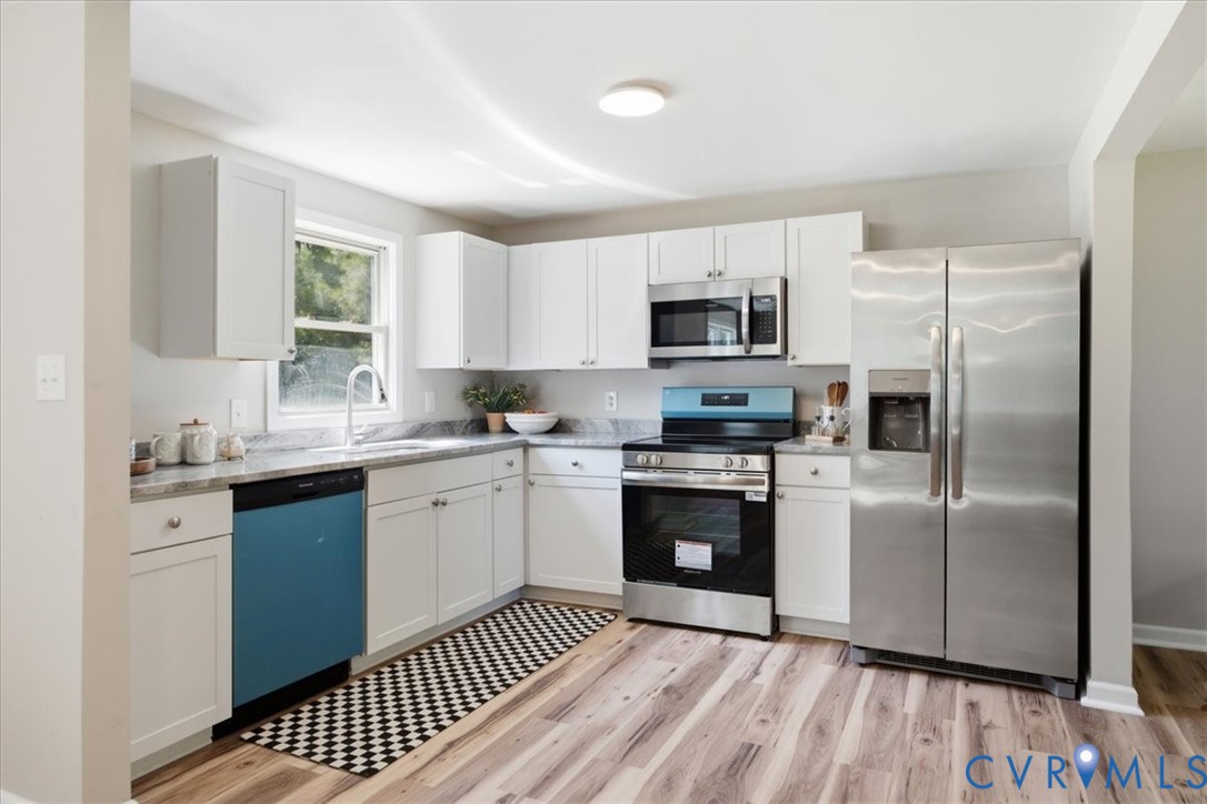 Modern kitchen with white cabinetry, stainless steel appliances, wood-finish flooring, and a window above the sink