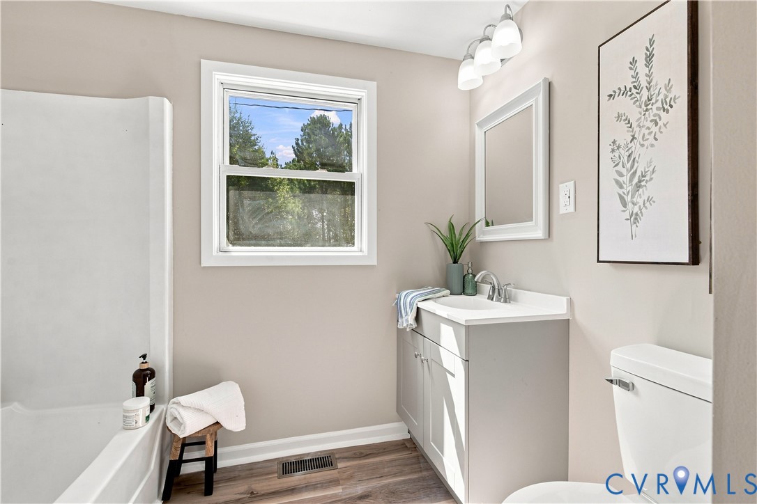Bathroom featuring wood-finish flooring, a white vanity with an integrated sink, a framed mirror, and a full-size bathtub
