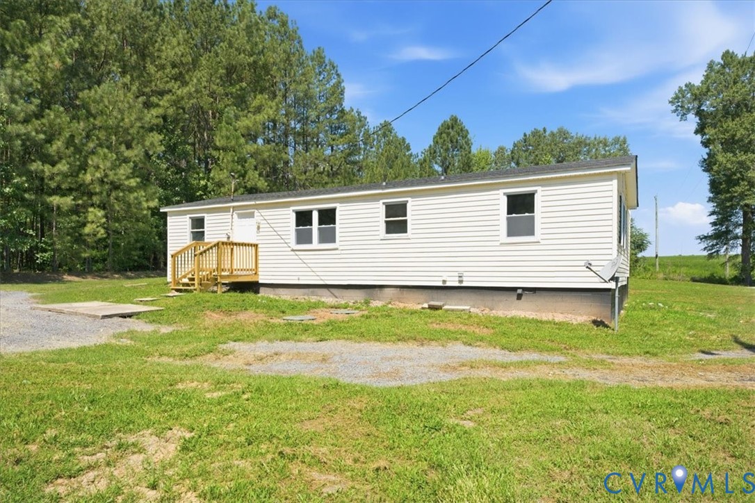 White horizontal siding, dark shingle roof, natural wood deck, and a gravel driveway