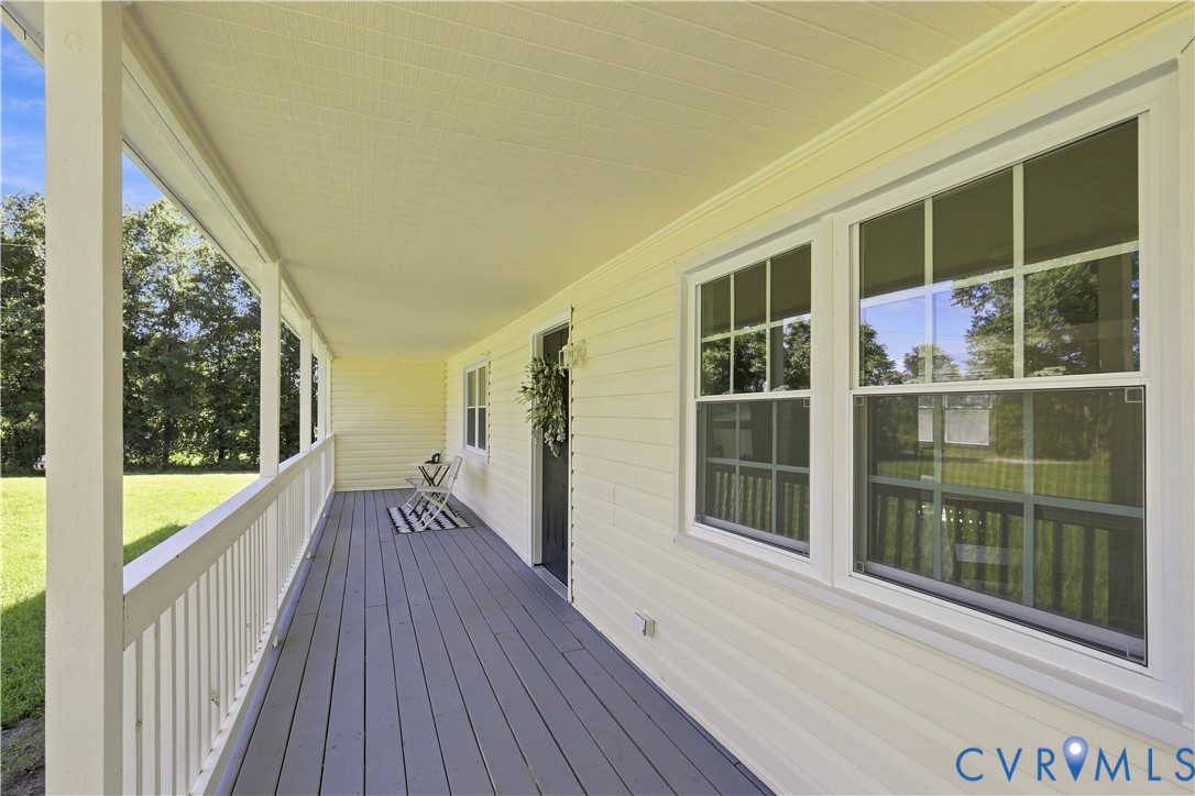 Expansive covered porch with a painted wood floor, white railing, and multiple windows