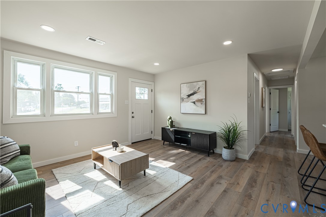Wood-finish flooring, recessed lighting, multiple windows, a paneled entry door, and a hallway with a ceiling light Wood-finish flooring, recessed lighting, multiple windows, a paneled entry door, and a hallway with a ceiling light