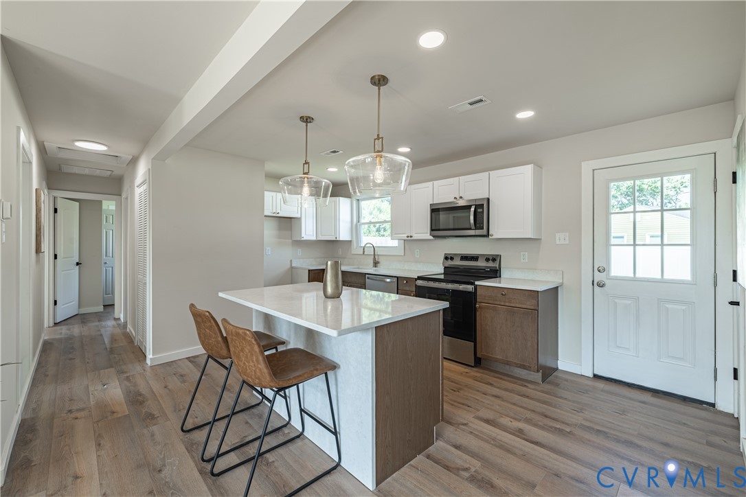 Kitchen featuring a central island with countertop seating, stainless steel appliances, recessed lighting, and wood-finish flooring Kitchen featuring a central island with countertop seating, stainless steel appliances, recessed lighting, and wood-finish flooring