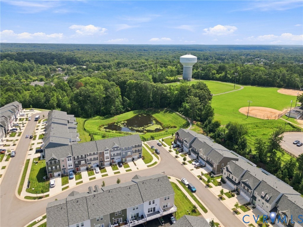Aerial representation of a residential community with multi-level townhomes, a pond, and expansive green spaces
