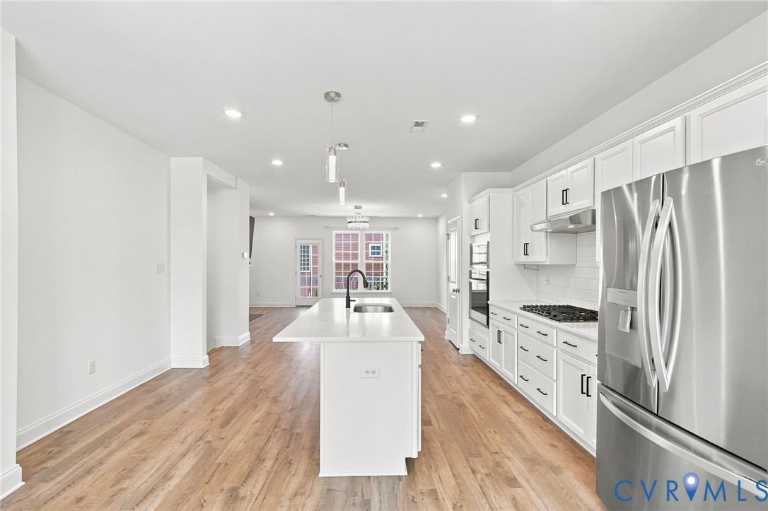 Kitchen with a center island, white cabinetry, stainless steel appliances, wood-finish flooring, and recessed lighting
