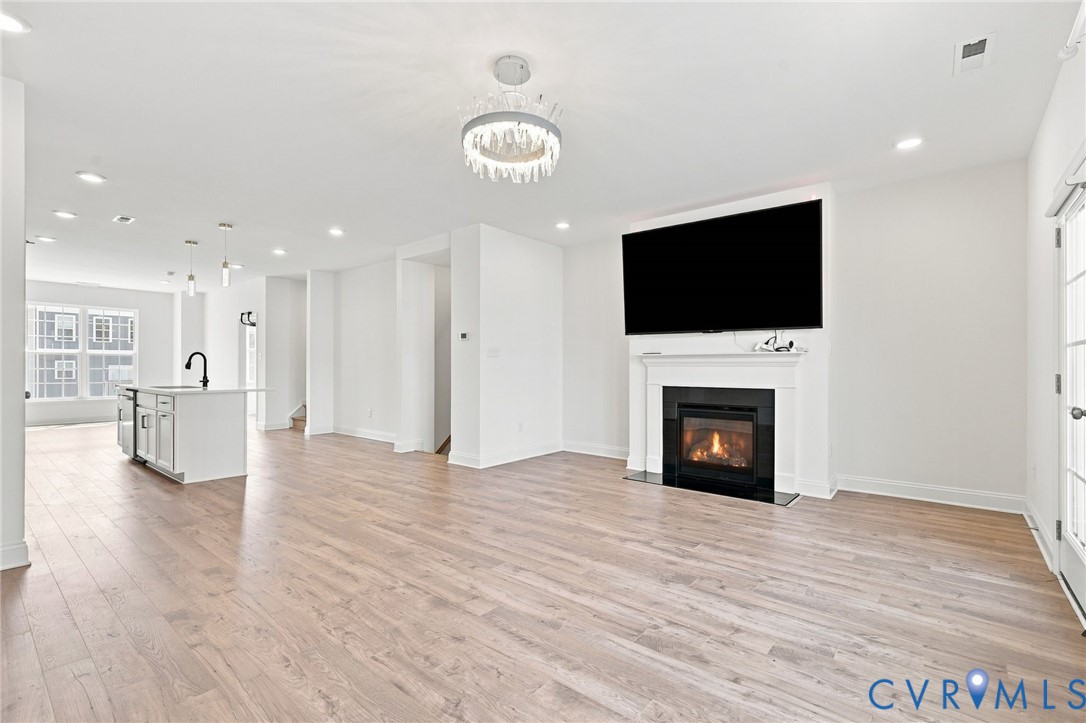 Expansive space featuring wood-finish flooring, a fireplace with a white mantel, and a kitchen island with pendant lighting