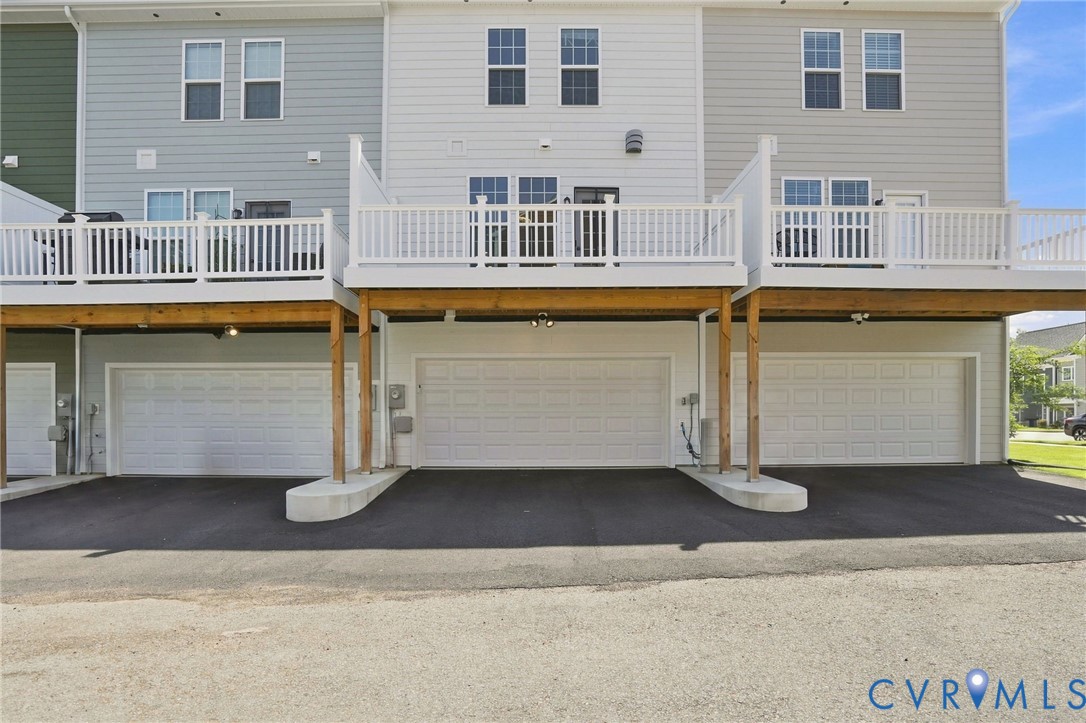 Rear exterior with multiple garages, upper-level decks with white railings, and light-toned siding
