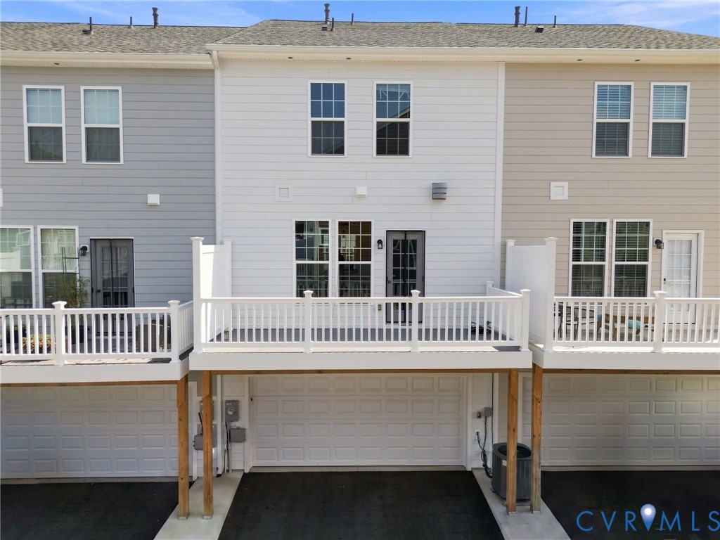Multi-level townhome featuring a rear deck with white railings, a ground-level garage, and a light-colored siding exterior