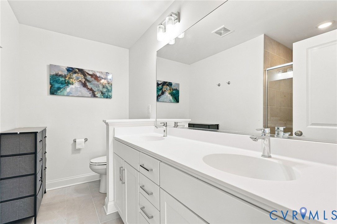 Dual vanity with integrated sinks and chrome fixtures, white cabinetry with silver-tone hardware, full-width mirror, and a tiled shower enclosure with a glass door