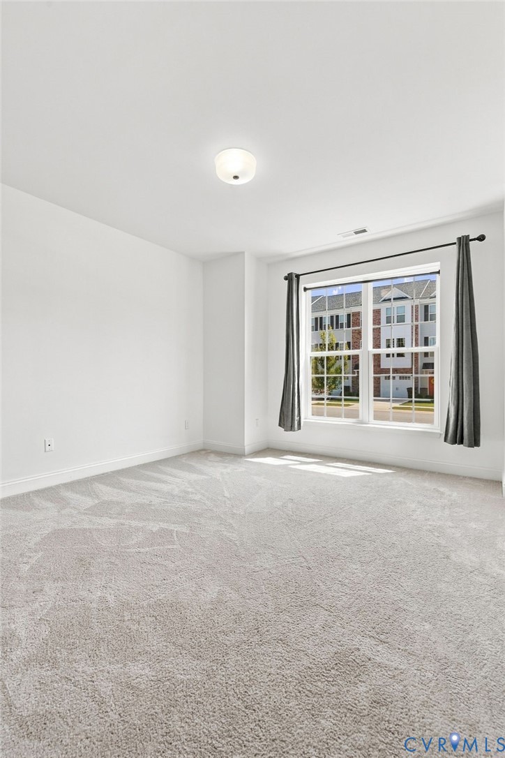 Neutral-toned carpeting, white walls, flush mount ceiling light, and a window with dark curtain rods