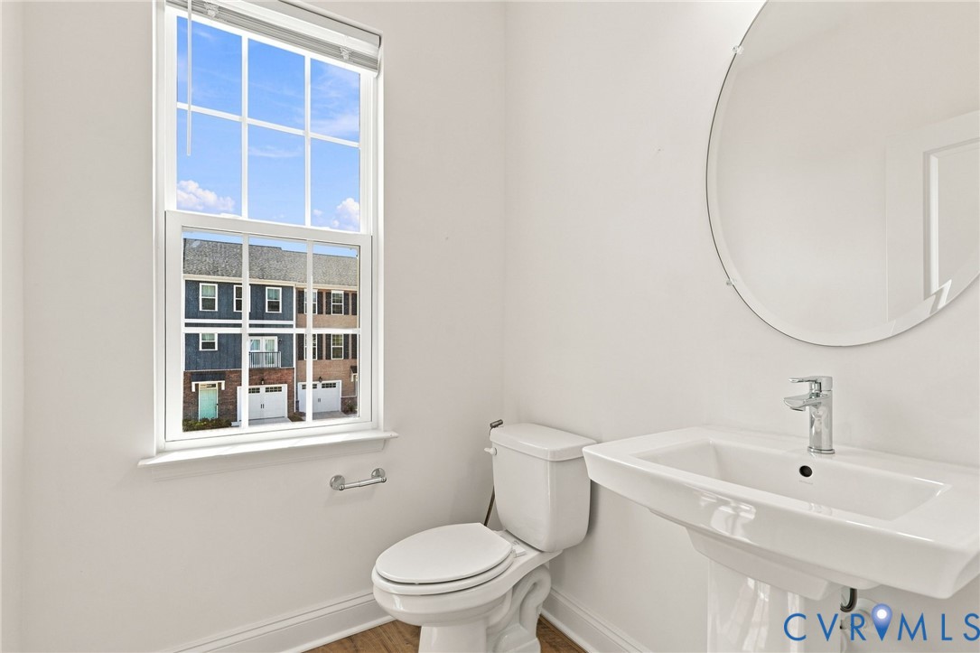 Pedestal sink with chrome faucet, oval frameless mirror, and a double-hung window