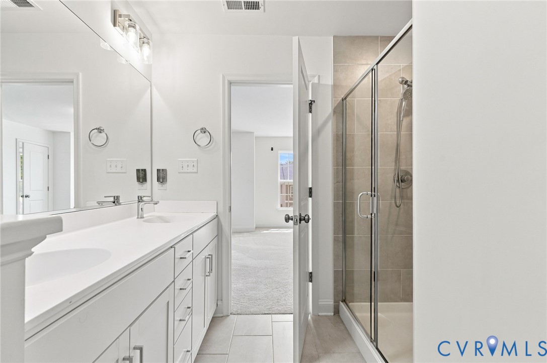 Dual vanity with integrated sinks, brushed nickel fixtures, contemporary lighting, and a glass-enclosed shower featuring tile surround