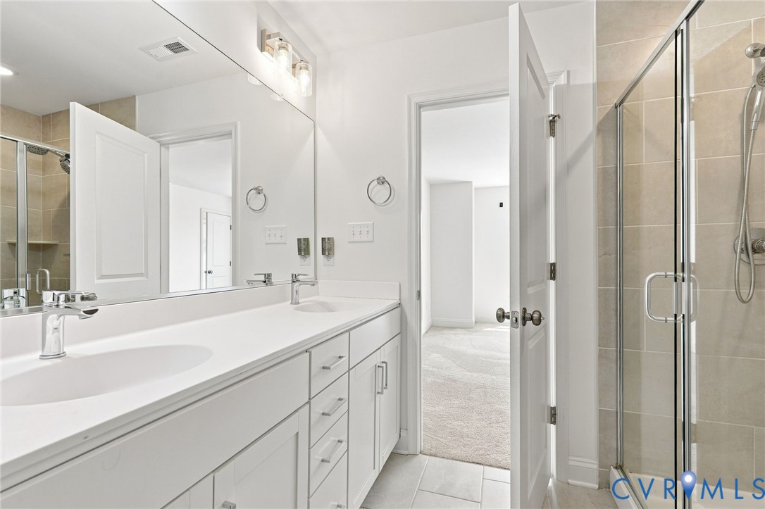 Dual vanity with white cabinetry and integrated sinks, a large wall-mounted mirror, and a glass-enclosed shower with tiled walls