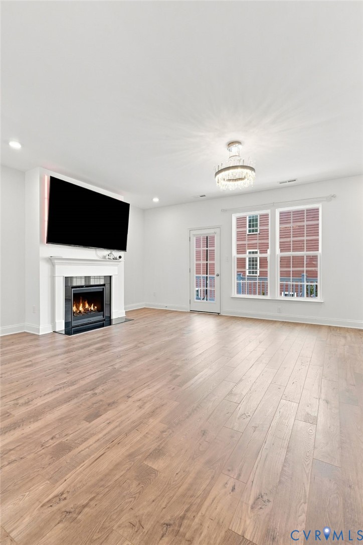 Spacious living area featuring wood-finish flooring, a fireplace with a white mantel, and a multi-pane window
