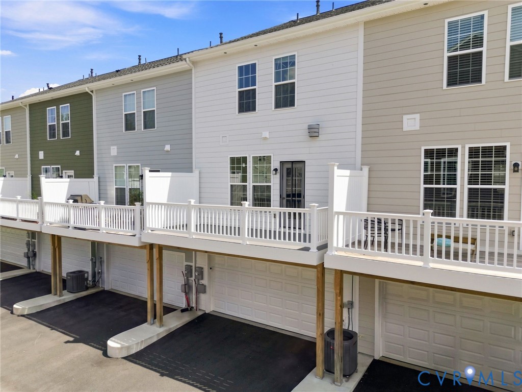 Multi-level townhome featuring white siding, private elevated deck with white railing, and an attached garage with paved driveway