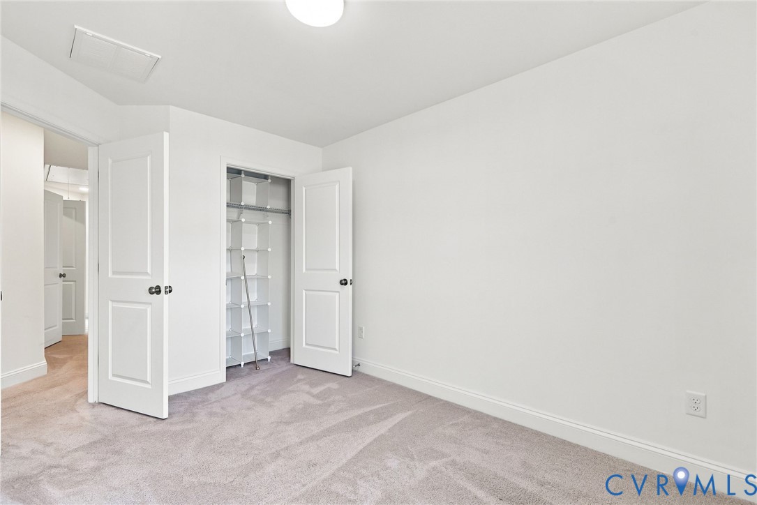 Plush carpet flooring, white walls, flush mount ceiling light, and a built-in closet with shelving