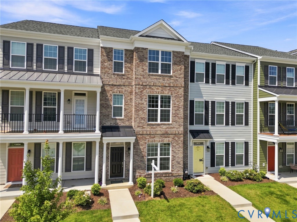 Brick facade, multi-story townhouse, covered entry, black shutters, and well-maintained landscaping