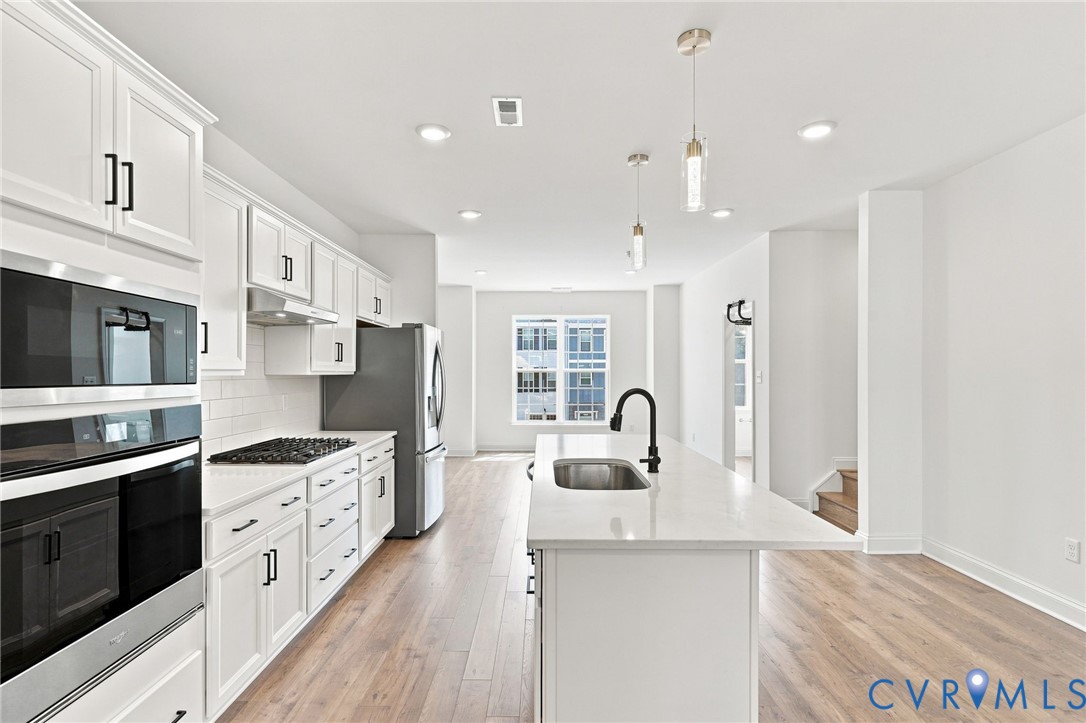 Bright kitchen featuring white cabinetry, integrated stainless steel appliances, a center island with sink, wood-finish flooring, and recessed lighting