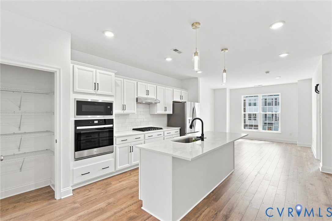 Kitchen featuring white shaker cabinets, stainless steel appliances, a center island with sink, and wood-finish flooring
