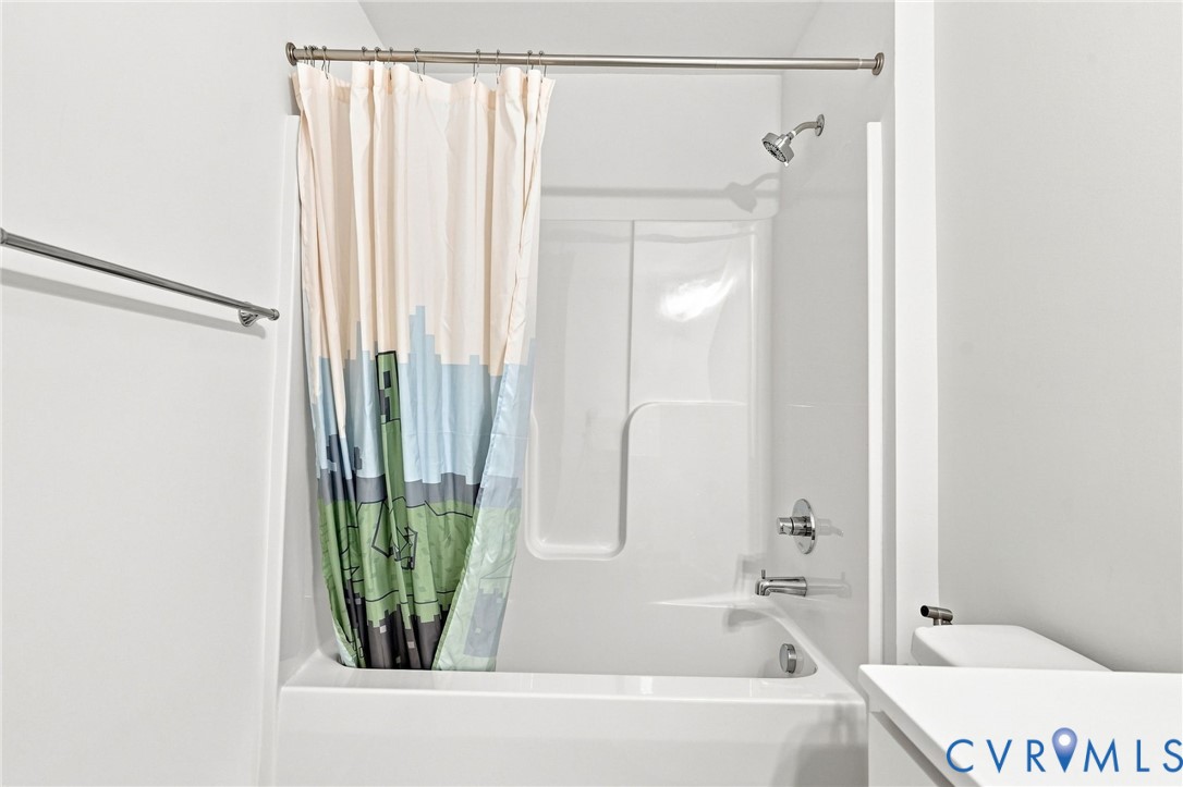 White bathtub with an integrated shower, chrome fixtures, and a shower rod